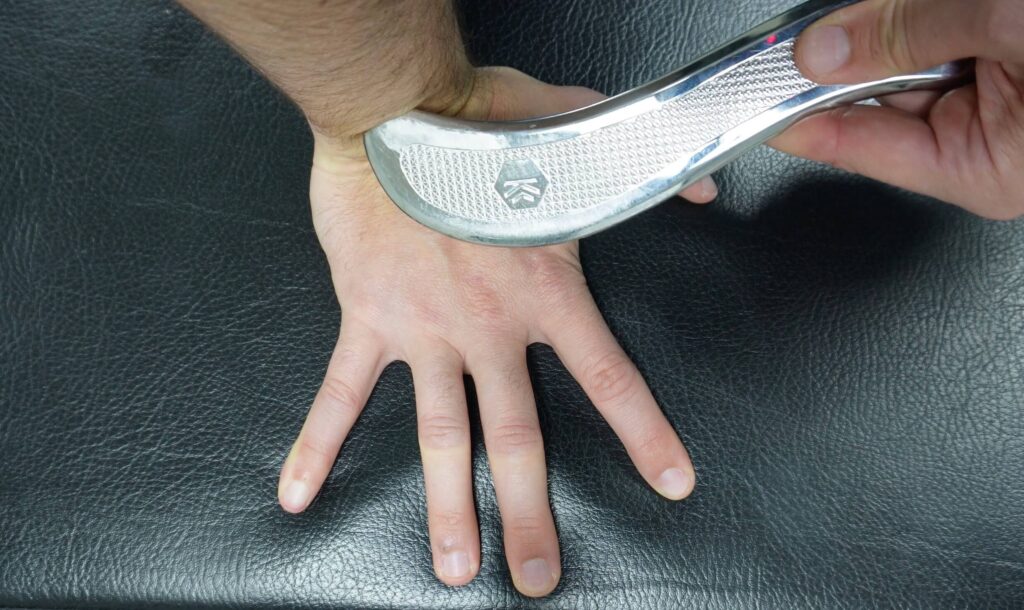 a photo from above of the wrist on a bench, palm down, in extension using a muscle scraper in the crease to break up scar tissue